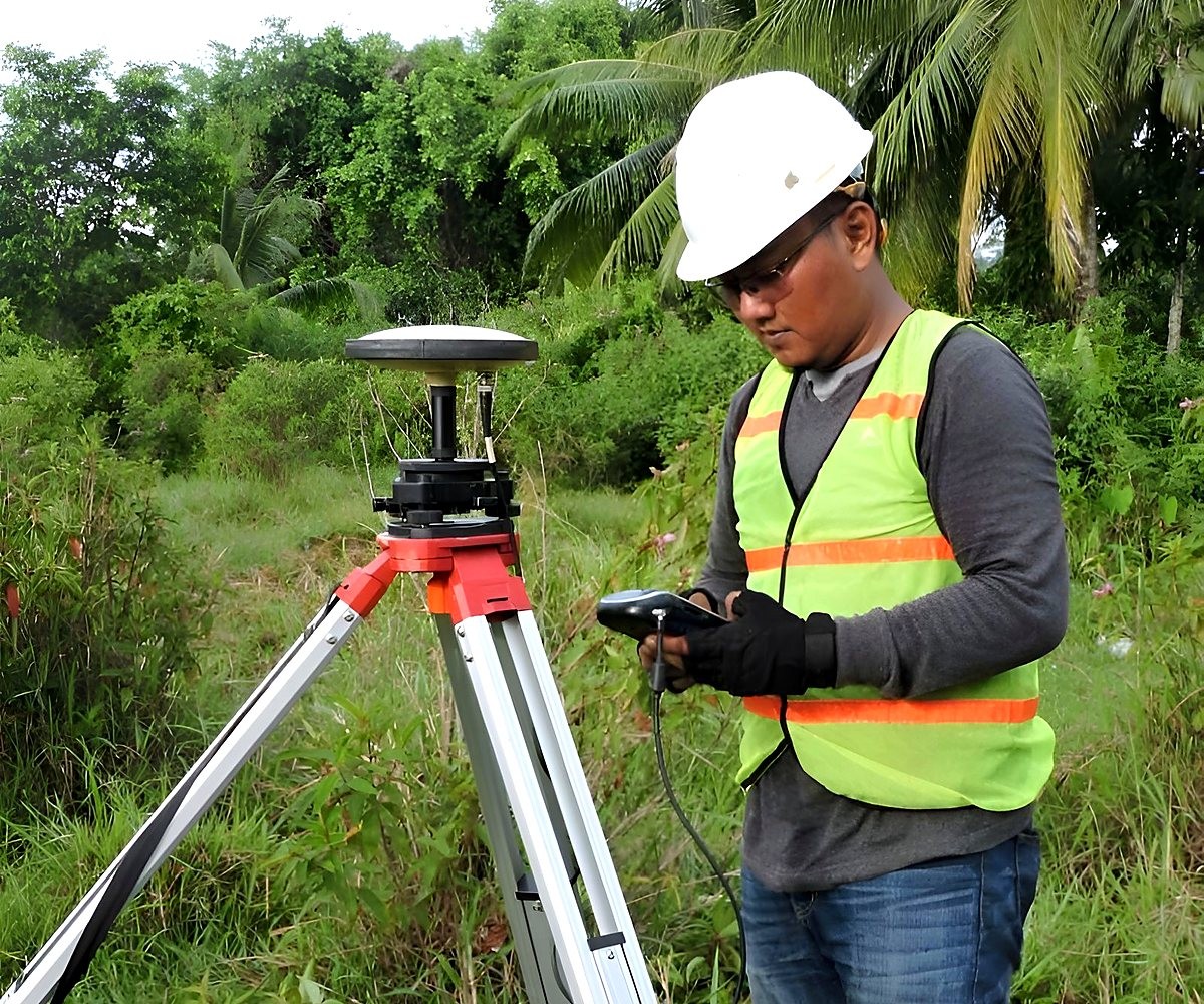 Profissional de capacete e colete refletivo ao lado de um equipamento de topografia sobre tripé